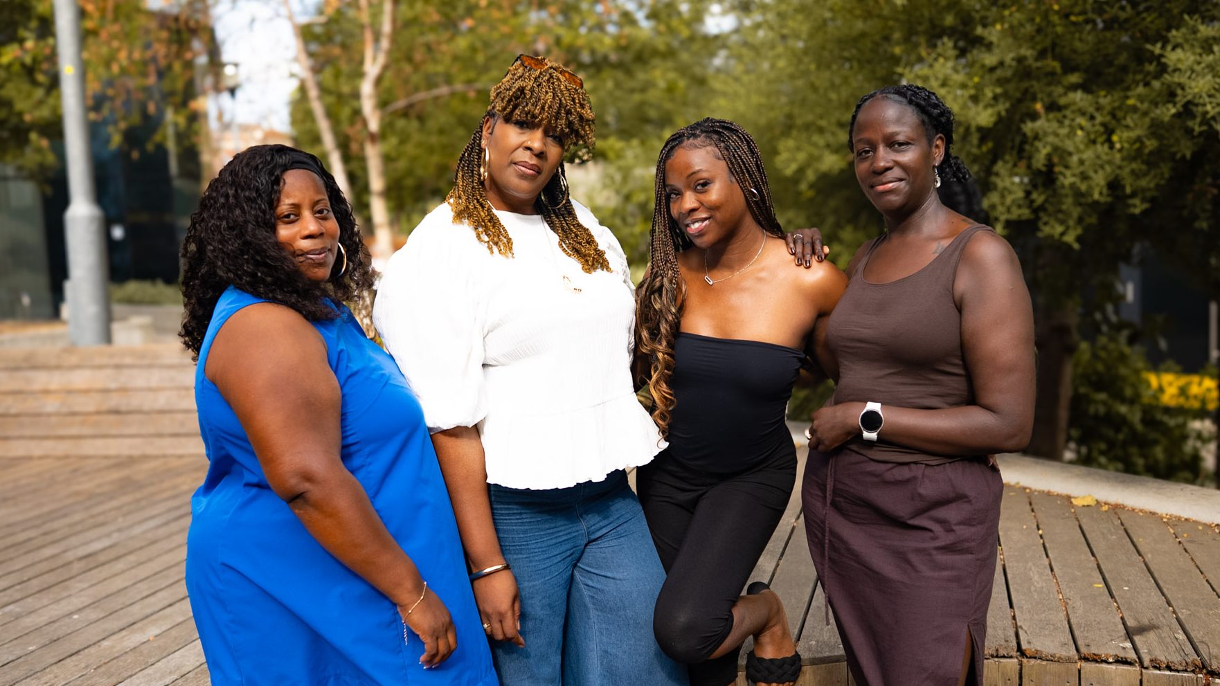 Four women standing together outdoors, smiling at the camera in a supportive group pose